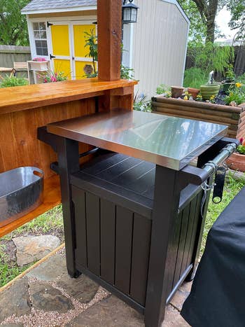 close up of reviewer's outdoor cart showing stainless steel top and hanging hooks on the paper towel bar