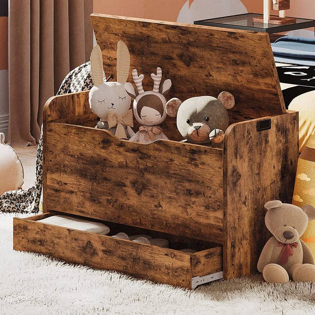 wooden bench at the foot of a child's bed. it is open and full of toys, with a slot at the bottom holding small shoes and linens. 