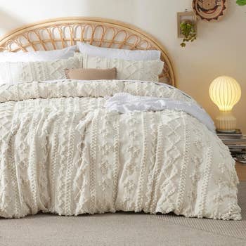 Cozy bedroom scene with a textured bedspread, rattan headboard, soft pillows, and a glowing table lamp