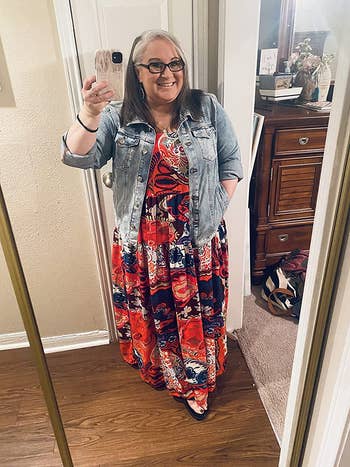 reviewer wearing the red floral dress with a denim jacket over it