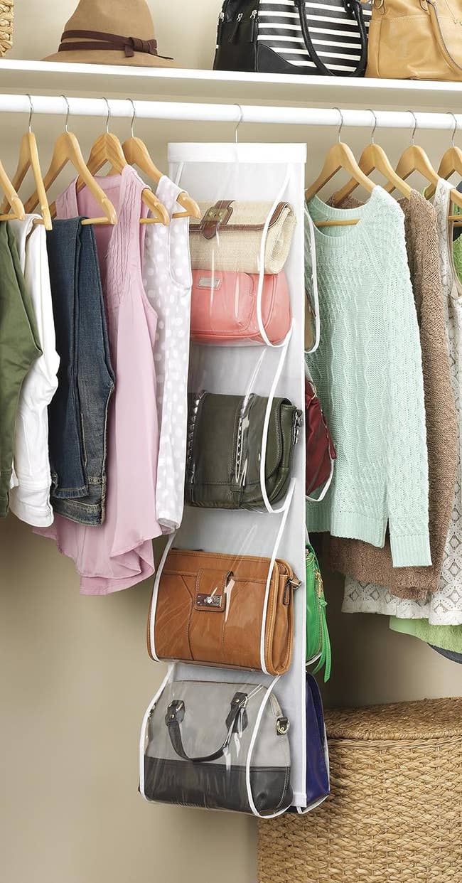 Hanging closet organizer with various compartments holding handbags and jeans, next to hanging clothes