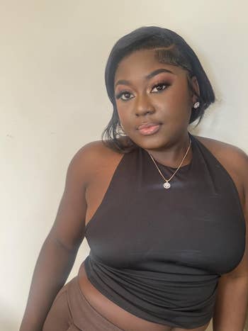 Person successful  a stylish achromatic  halter apical  and brownish  pants, wearing elegant constitution  and a necklace, posing against a neutral background