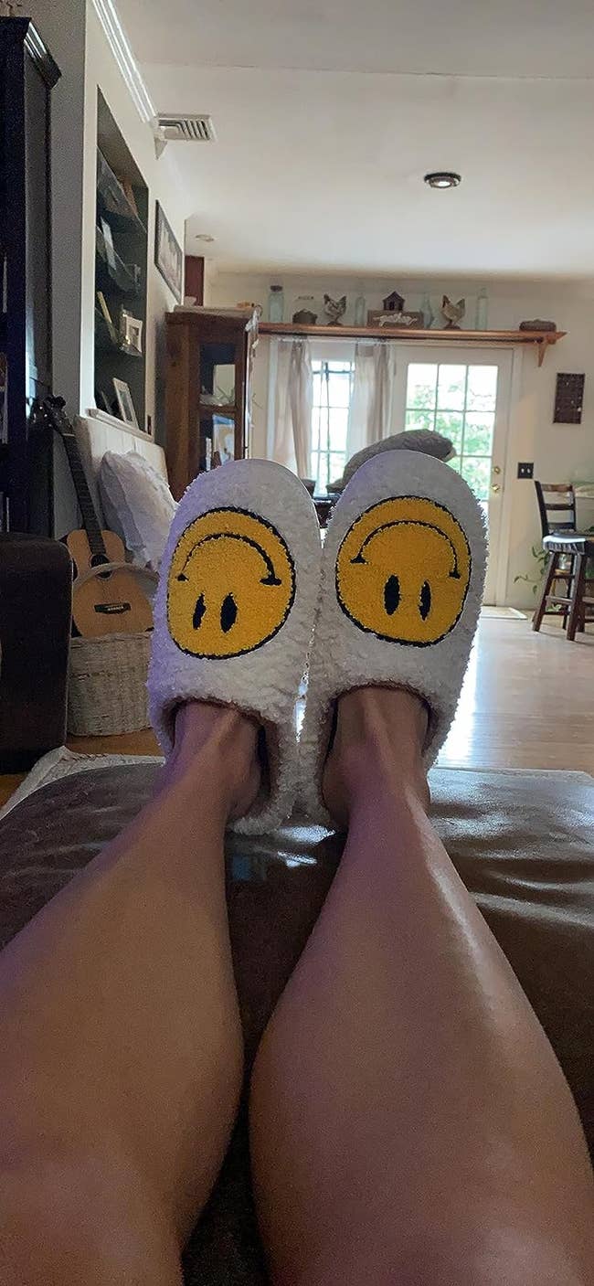 A reviewer wearing the white slippers with yellow smiley faces