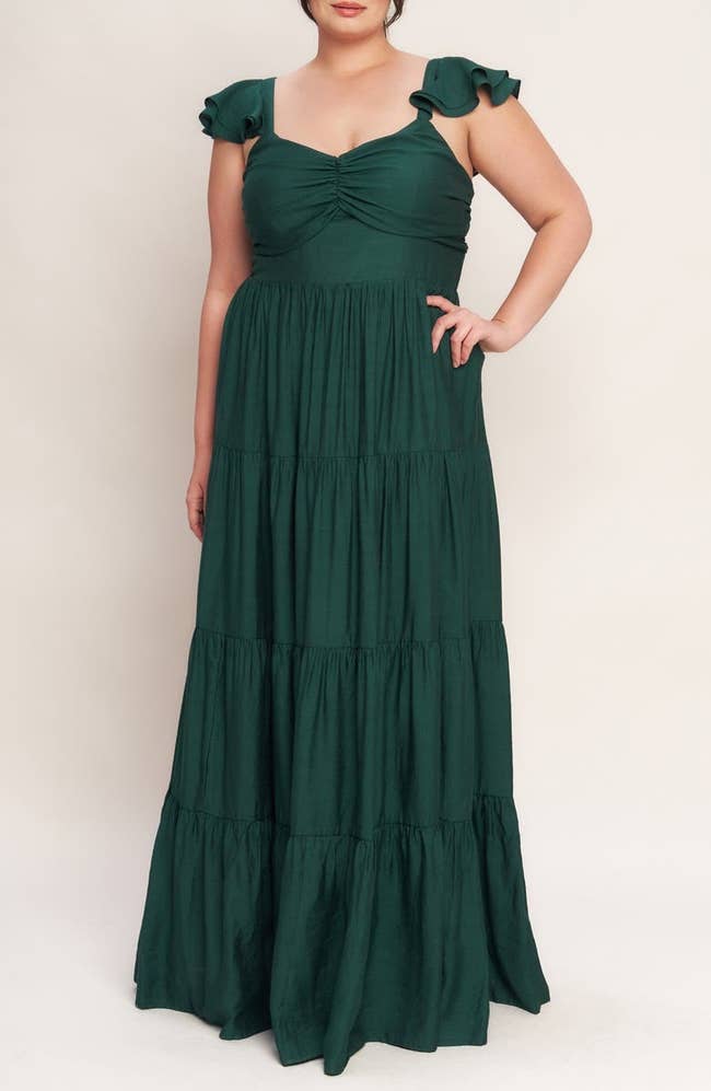 Person in a flowing, tiered maxi dress with ruffled sleeves, ideal for occasions; standing with one hand on hip against a plain background
