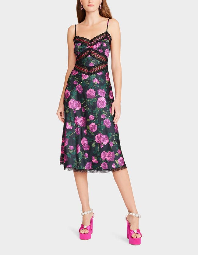 model wearing black spaghetti strap dress with lace detail and pink roses on it