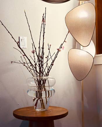 Vase with budding branches on a wooden table, flanked by a modern wall lamp