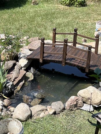 Small backyard pond with a woody  bridge, surrounded by rocks and plants, creating a serene outdoor space