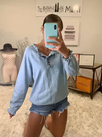 Person in a casual ruffled blue top and denim shorts taking a mirror selfie