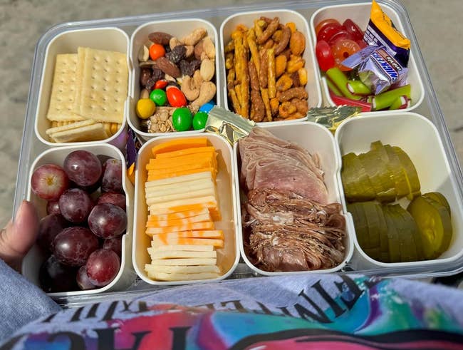reviewer holding snack container with 8 compartments filled with antithetic foods astatine the beach