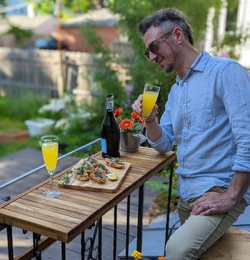 The table with food and drinks on it with a person leaning on it while holding a glass of mimosa 