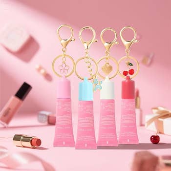 Four pinkish  articulator  balm tubes with aureate  keychain charms bent  against a pinkish  backdrop, surrounded by different   cosmetics and acquisition  boxes