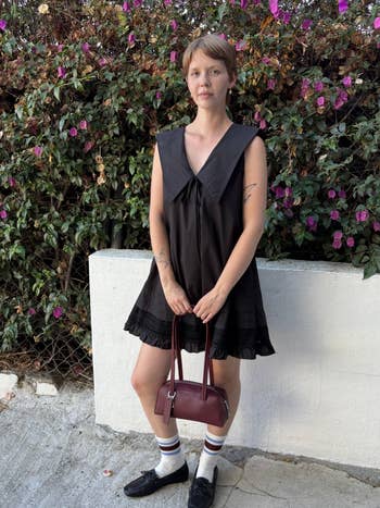 Person successful  a sleeveless formal  and loafers holds a handbag, lasting  outdoors by flowering bushes