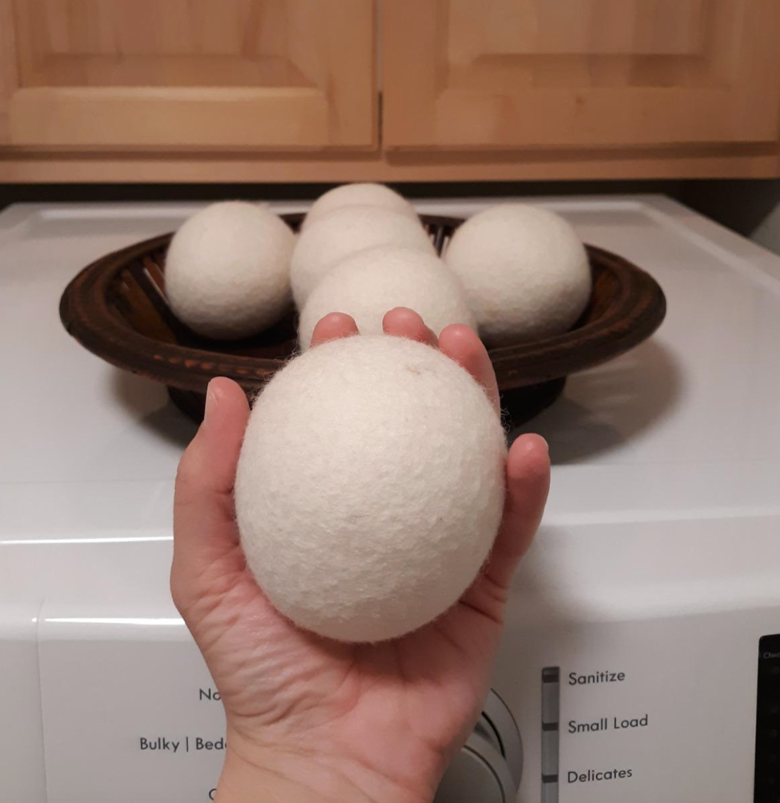 Reviewer holding a white dryer ball beside a dryer 