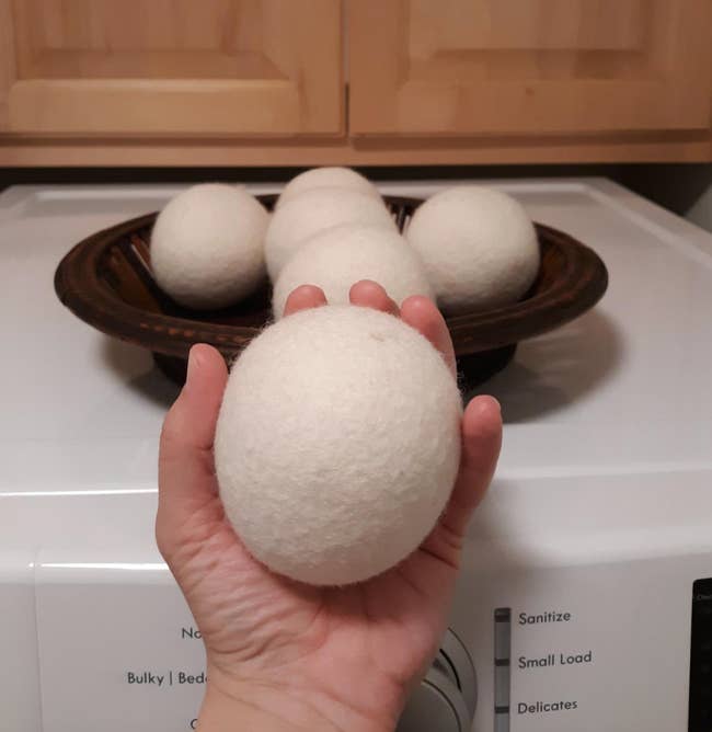 Reviewer holding a white dryer ball beside a dryer 