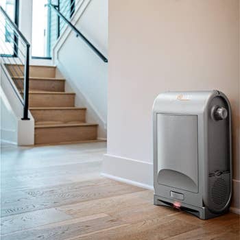 Compact home air purifier placed on a wooden floor near a staircase. Sleek and modern design suggests it fits well in contemporary homes