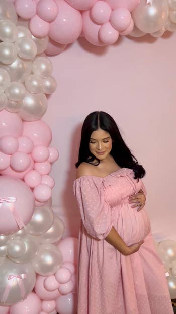 Person successful  a flowing formal  stands beside a decorative balloon arrangement, cradling their babe  bump