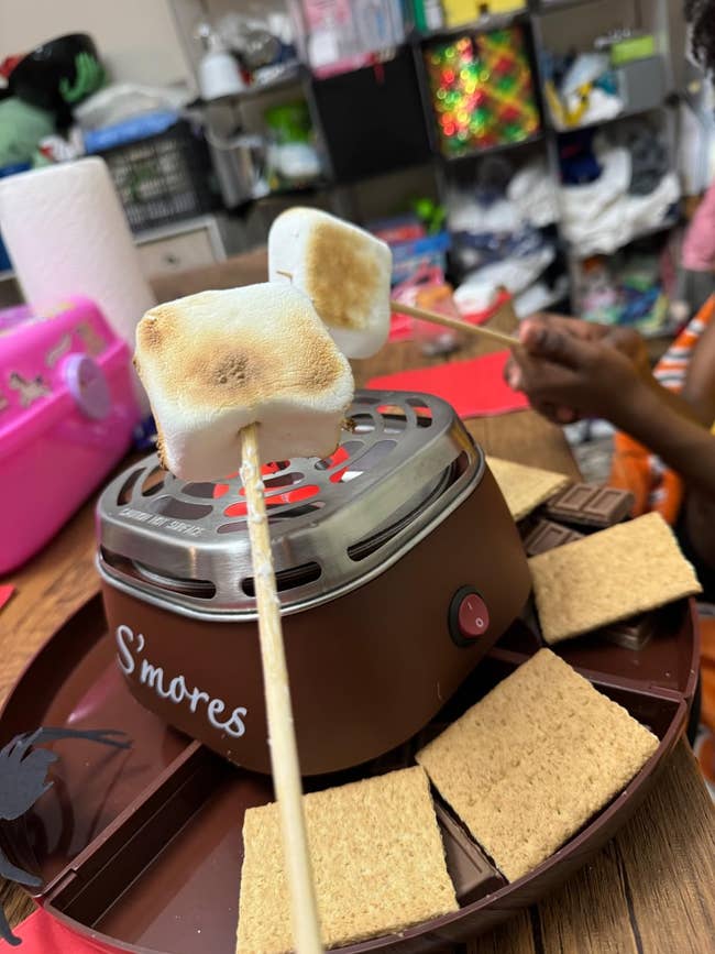 Portable s'mores shaper  successful  usage  with marshmallows connected  sticks and graham crackers connected  a tray, acceptable   up   for a cozy indoor snack
