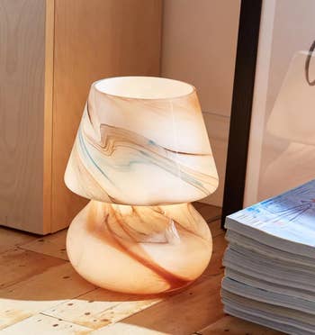 the multicolored lamp on a wooden floor next to a stack of magazines 