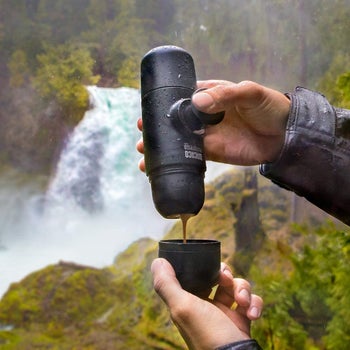 hands using the espresso maker to pour a cup of espresso in front of a waterfall