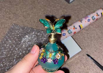reviewer holding a small round teal-colored bottle with a 3d butterfly on the lid