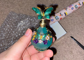 reviewer holding a small round teal-colored bottle with a 3d butterfly on the lid
