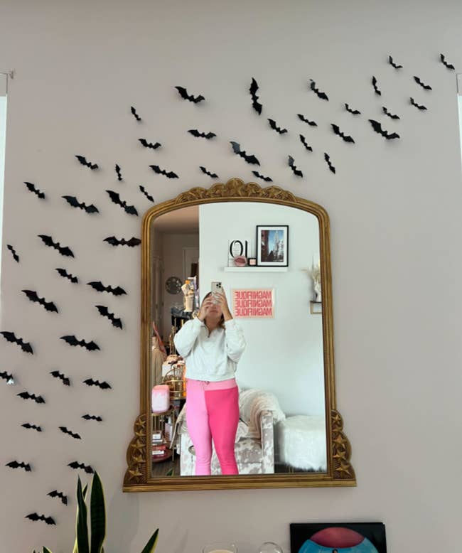 writer Ali after putting up bats around her gold wall mirror in her apartment