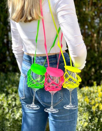 Model with neon strapped wine glass holders in pink, green, and yellow attached to their shoulder