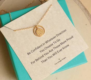 Gold compass necklace on display card with inspirational quote, ideal for gift giving