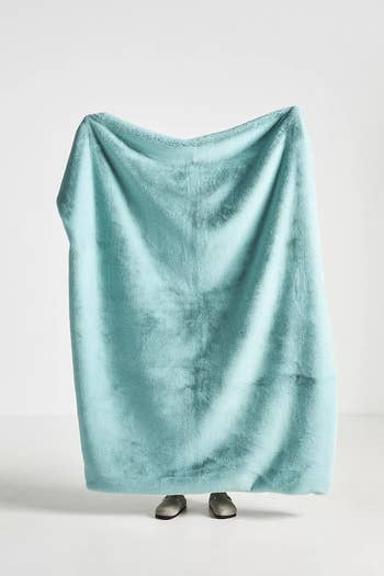model holding up a teal-colored blanket showing it's longer than them