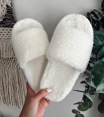 Person holding plush white open-toed slippers 
