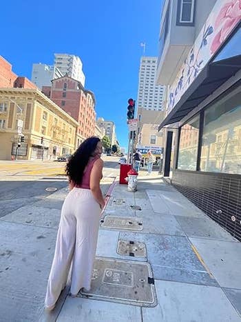 A reviewer in loose pants walks on city sidewalk, glancing back. Urban buildings and traffic light visible