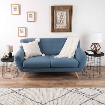 A modern blue sofa with cushions and a throw blanket in a living room setting with decorative items and wall art