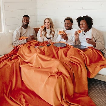 four adults sharing an orange throw blanket on a couch