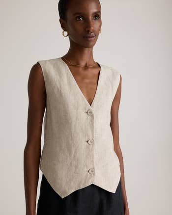 Person wearing a sleeveless beige button-up vest with V-neck and hoop earrings, suitable for a stylish, minimalist look