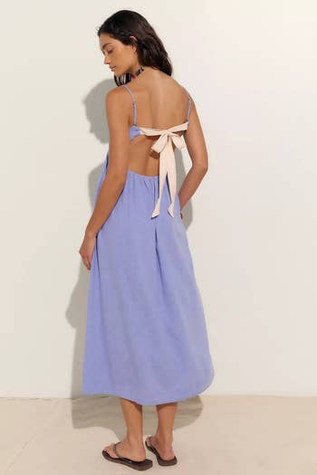 Person wearing a backless, sleeveless midi dress with a tied bow, styled casually with sandals, suitable for summer or beach outings