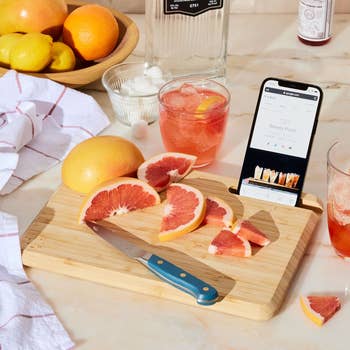 a chopped grapefruit on a cutting board that has a slot which is holding a smartphone