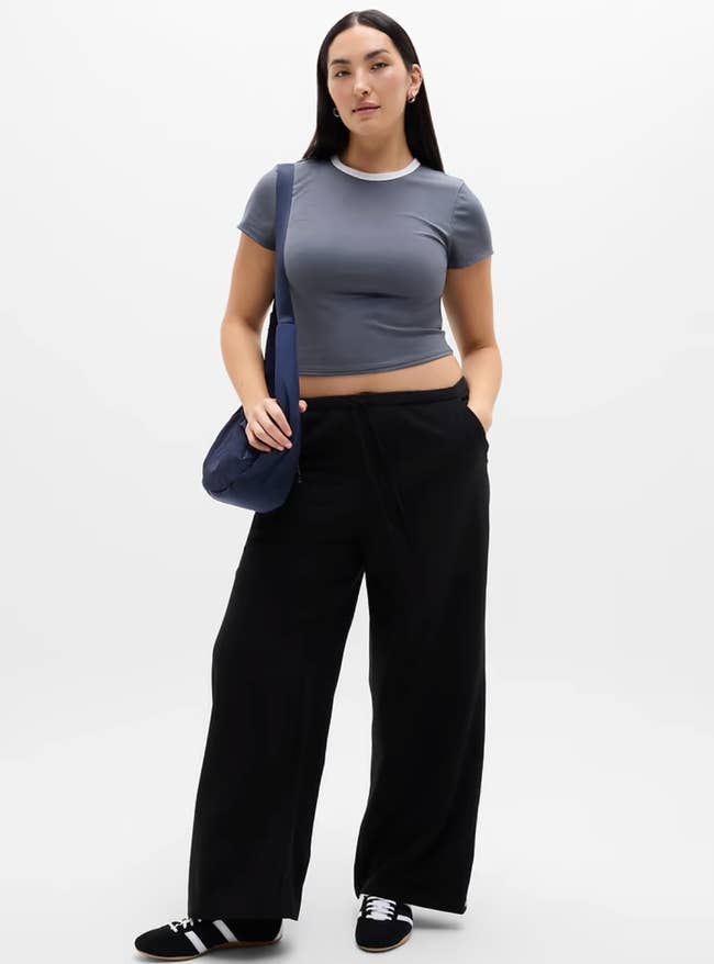 Person successful a fitted harvest top, wide-legged pants, and sneakers, carrying a enarthrosis bag, modeling a casual, sporty outfit