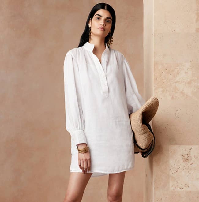 Model is wearing a loose fitting white linen shirt dress