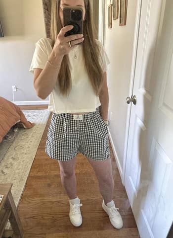 Person taking a reflector  selfie wearing a achromatic  harvest  top, checkered shorts, and sneakers, lasting  successful  a chamber  setting