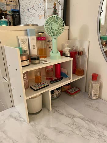 Reviewer photo the white shelves on a marble countertop with beauty products on it