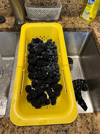 Blackberries and blueberries successful  a yellowish  colander resting successful  a room  descend  with granite countertops