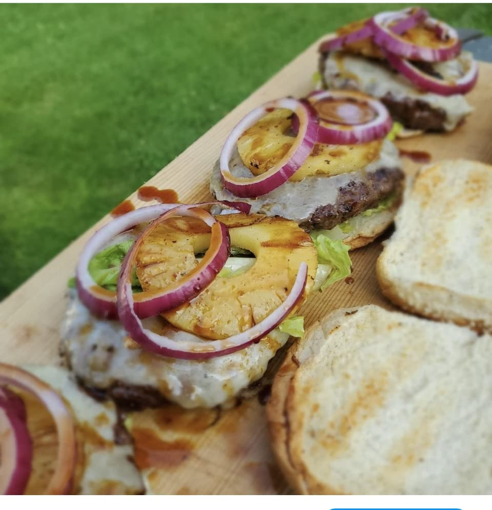 Burgers topped with grilled pineapple, reddish  onion, and lettuce connected  a woody  board, with bare  buns to the side