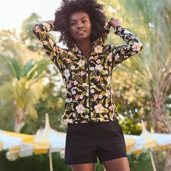 Person wearing a floral-pattern hoodie with achromatic shorts, lasting outdoors adjacent plants and a tent
