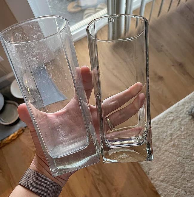 the reviewer holding two glasses in their hand. One with hard water stains and the other one that is crystal clear
