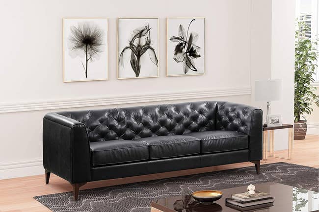 Elegant black tufted leather sofa in a stylish living room setting with wall art and décor accents. Perfect for a chic home update
