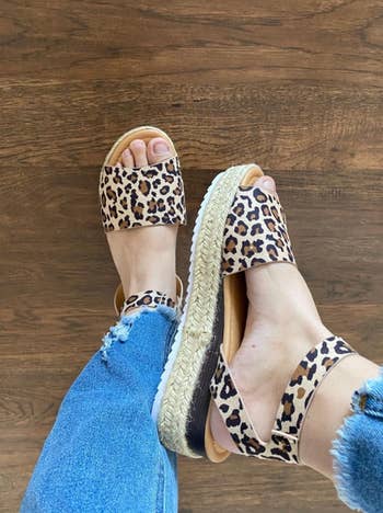 reviewer wearing leopard print sandals with espadrille soles, paired with distressed blue jeans