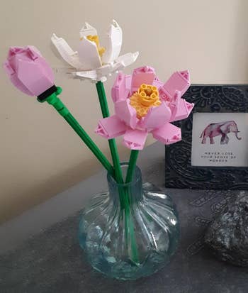 Three LEGO flowers in a clear vase are arranged next to a framed image of an elephant and a quote saying, 