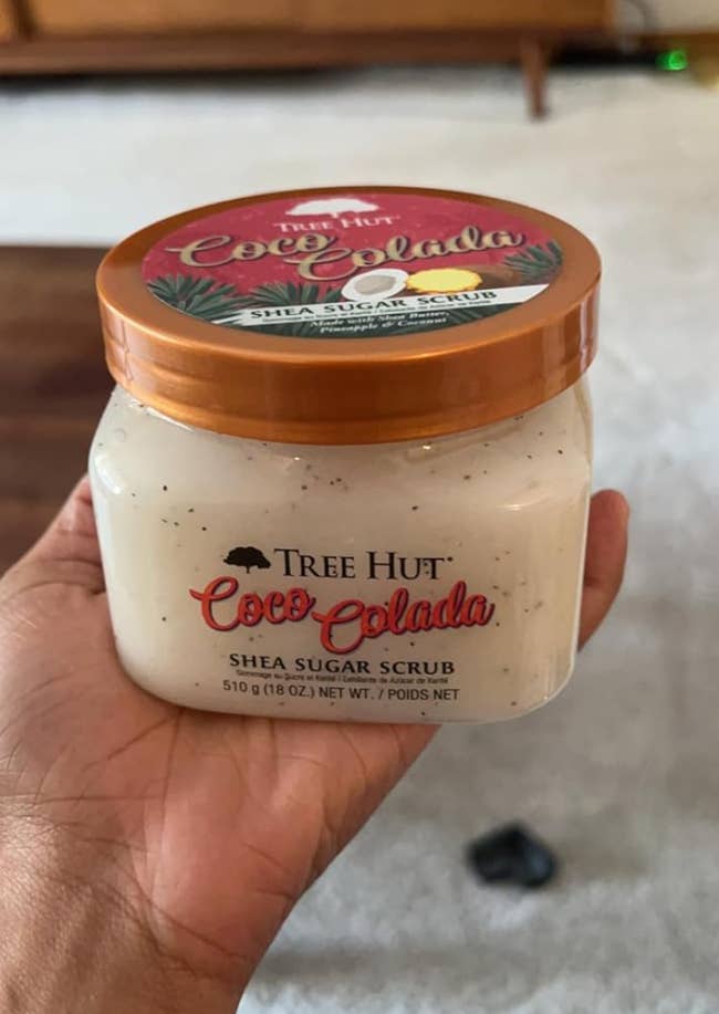 A person holds a jar of Tree Hut Coco Colada Shea Sugar Scrub, showing the front label closely