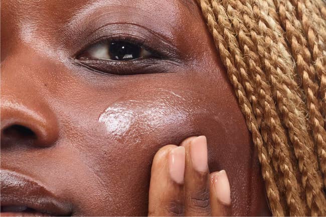 dark skin model rubbing clear sunscreen onto cheek 