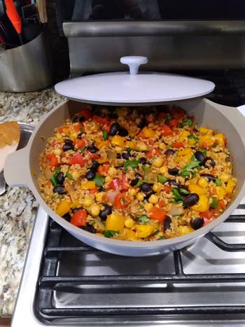 A pot of mixed grain and vegetable dish with corn, black beans, tomatoes, and herbs, placed on a stove in a kitchen setting